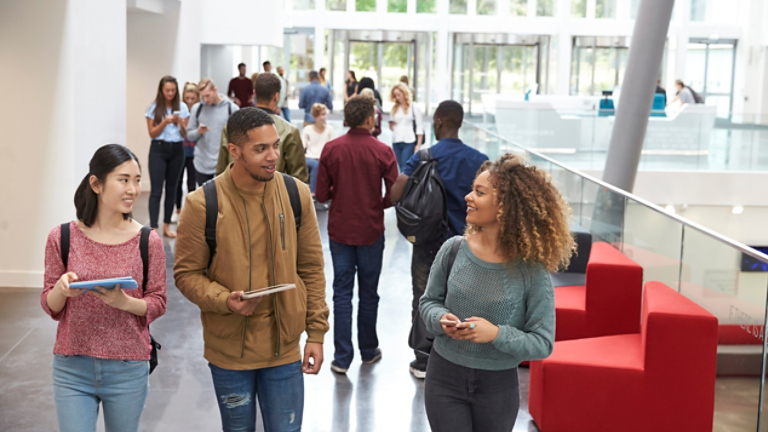 Students holding tablets and phone talk in university lobby
