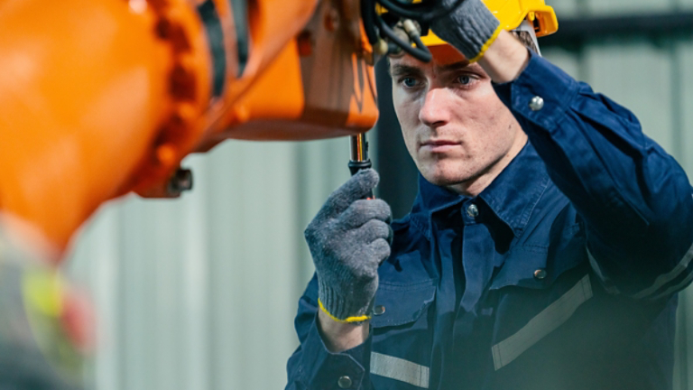Young technician repairs an industrial robotic arm in a manufacturing facility