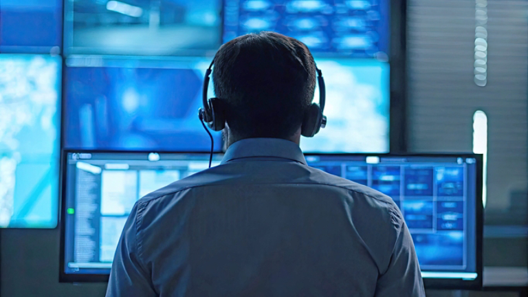 Cybersecurity risk management concept A person in a headset monitors multiple screens in a control room setting.