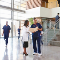 Two healthcare workers talk in the lobby of a busy hospital