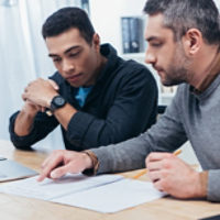 concentrated male coworkers using laptop and working with papers in office  