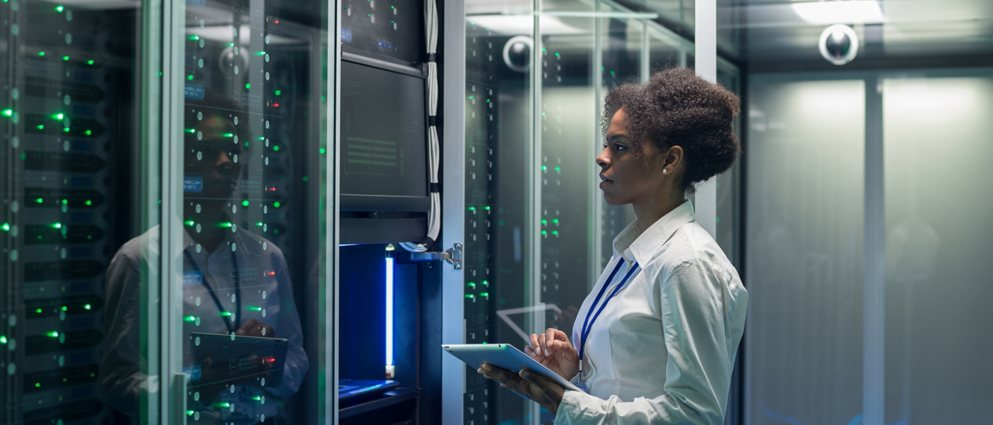 Medium shot of female technician working on a tablet in a data center full of rack servers running diagnostics and maintenance on the system