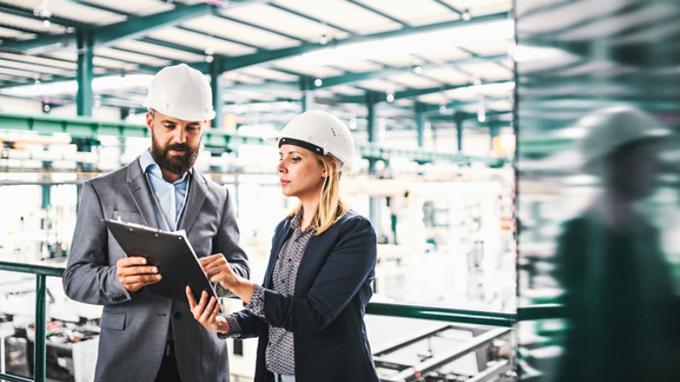 A portrait of an industrial man and woman engineer with clipboard in a factory.