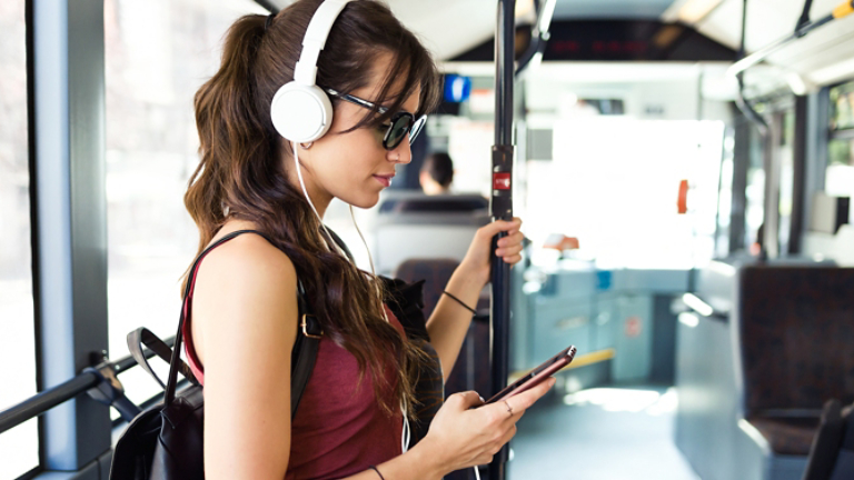 Shot of concentrated young student woman listening to music with mobile phone at the bus.