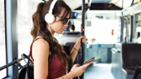 Shot of concentrated young student woman listening to music with mobile phone at the bus.