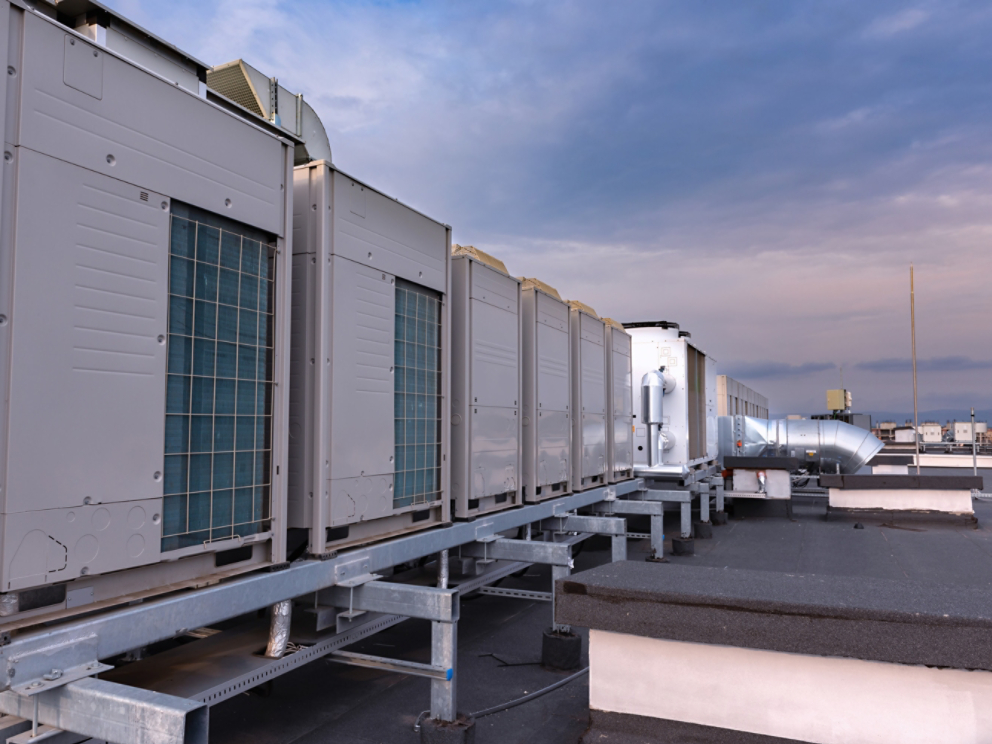Air conditioner units VRV (HVAC), big fan and a water cooler on a roof of new industrial building with blue sky and clouds in the background.