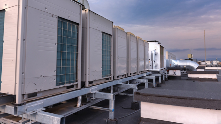 Air conditioner units VRV (HVAC), big fan and a water cooler on a roof of new industrial building with blue sky and clouds in the background.