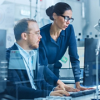 Modern Electronics Factory: Female Supervisor Talks to a Male Electrical Engineer who Works on Computer with CAD Software. Developing PCB, Microchips, Semiconductors and Telecommunications Equipment