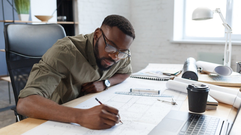 Afro-American architect working in office with blueprints.Engineer inspect architectural plan, sketching a construction project. Portrait of black handsome man sitting at workplace. Business concept
