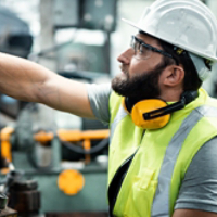 Men industrial engineer wearing a white helmet while standing in a heavy industrial factory behind. The Maintenance looking of working at industrial machinery and check security system setup in fact
