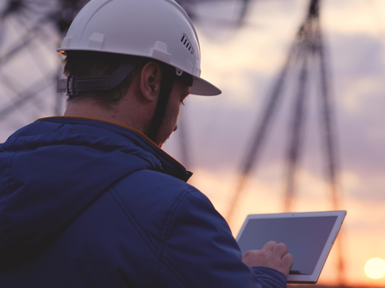 An electrician works in a tablet against a background of energized electrical towers, an engineer measures the level of current, an electrical network to supply light