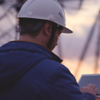 An electrician works in a tablet against a background of energized electrical towers, an engineer measures the level of current, an electrical network to supply light