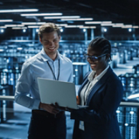 Data Center Female System Administrator and Male IT Specialist talk, Use Laptop. Information Technology Engineers work on Cyber Security Protection in Cloud Computing Server Farm.