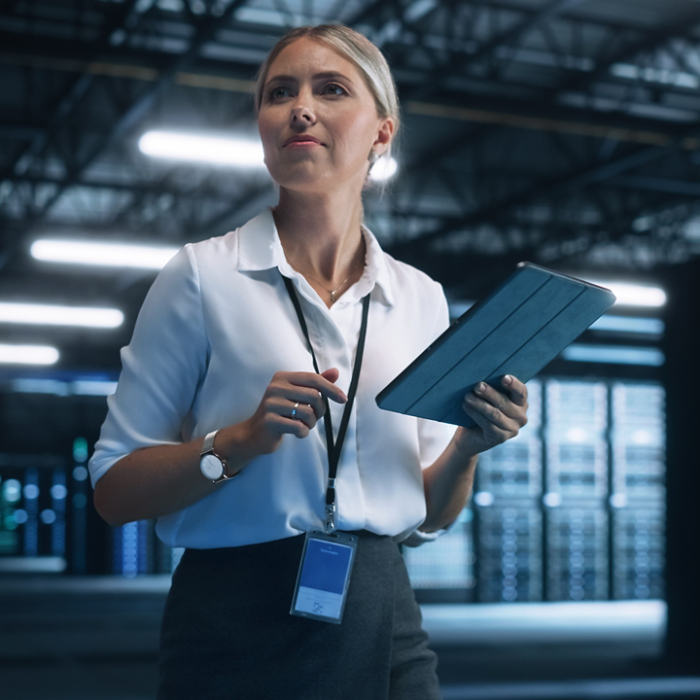 Data Center Female e-Business Entrepreneur Use Tablet Computer with Pleasure Smile. Information Technology Engineer and System Administrator work in Big Cloud Computing Server Farm.