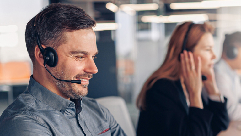 Smiling businessman in headphones talking online with client sitting in office