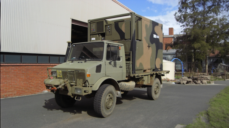 Side view of camouflage Klinge 10-Foot Refrigerated Conex Box on a military truck