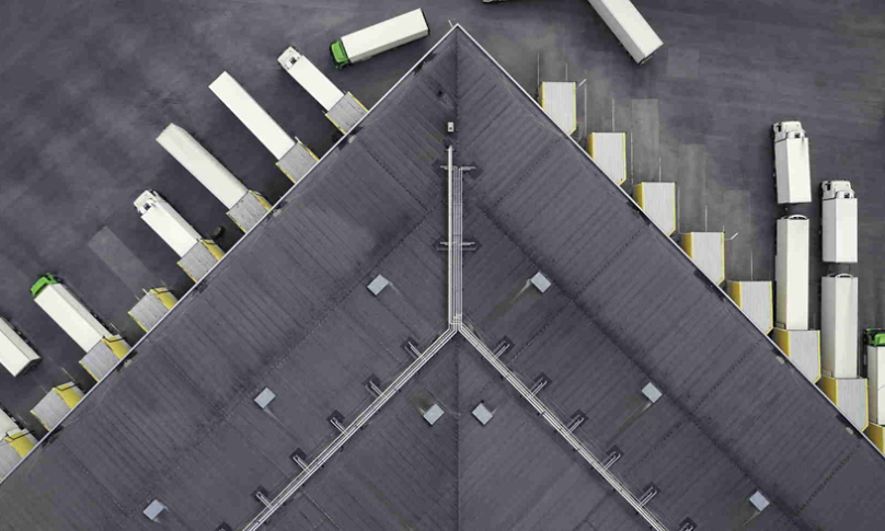 Aerial view of a large distribution warehouse with loading docks and many trucks.