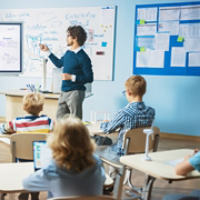 Elementary School Science Teacher Uses Interactive Digital Whiteboard to Show Classroom Full of Children how Software Programming works for Robotics. Science Class, Curious Kids Listening Attentively