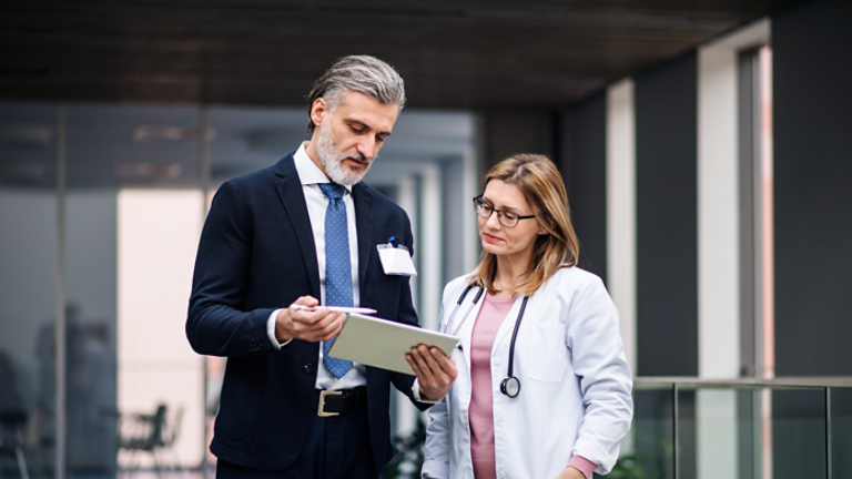 Pharmaceutical sales representative with tablet talking to doctor.