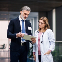 Pharmaceutical sales representative with tablet talking to doctor.