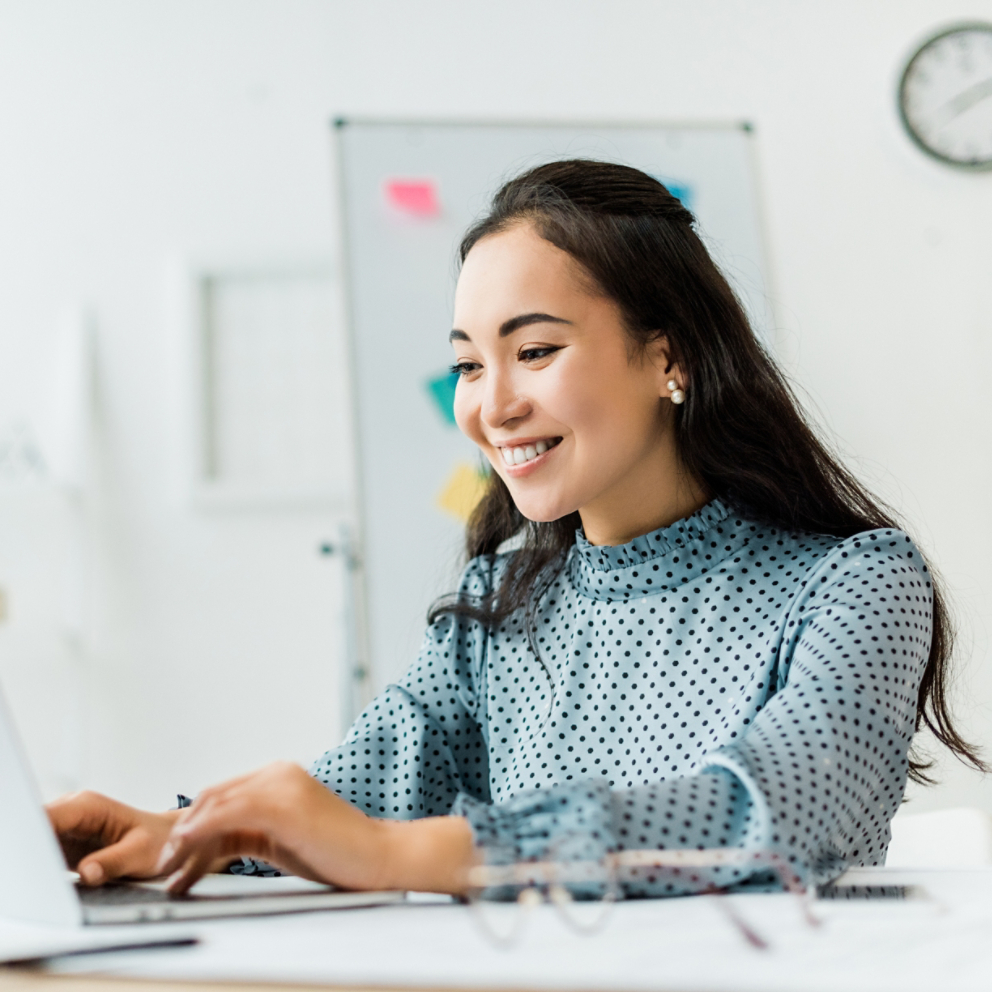 beautiful smiling asian businesswoman sitting at desk and using laptop in office