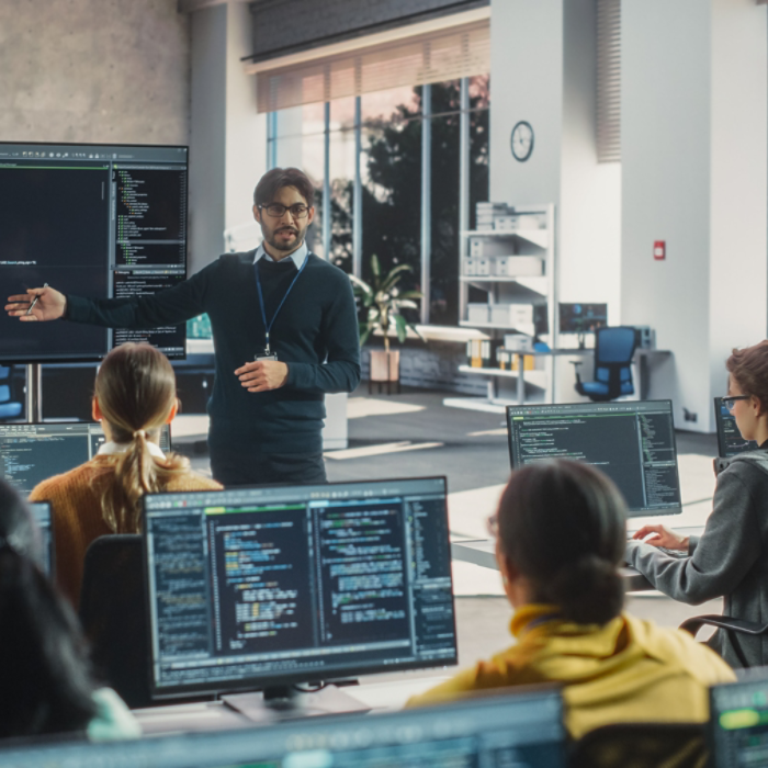 Knowledgeable Teacher Giving a Lecture About Software Engineering to a Group of Smart Diverse University Students. International Undergraduates Sitting Behind Desks with Computers