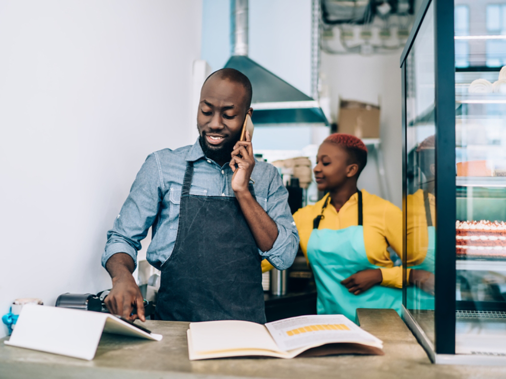 Owner of confectionery shop standing at counter and talking on phone