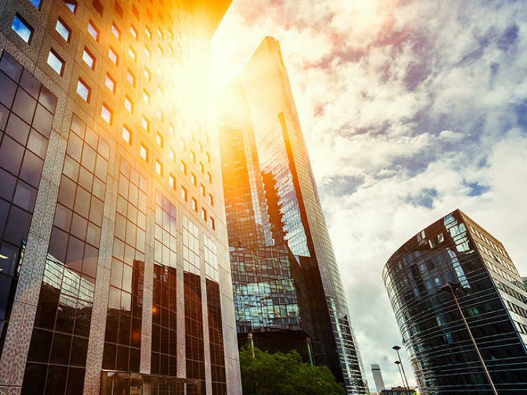 Skyscraper glass facades on a bright sunny day with sunbeams in the blue sky. Modern buildings in business district. Economy, finances, business activity concept. Bottom up view