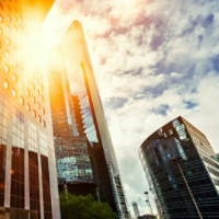 Skyscraper glass facades on a bright sunny day with sunbeams in the blue sky. Modern buildings in business district. Economy, finances, business activity concept. Bottom up view