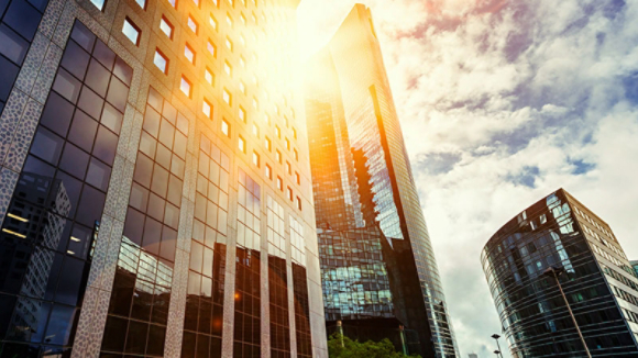 Skyscraper glass facades on a bright sunny day with sunbeams in the blue sky. Modern buildings in business district. Economy, finances, business activity concept. Bottom up view