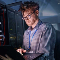 Focused male IT technician working at laptop in dark server room