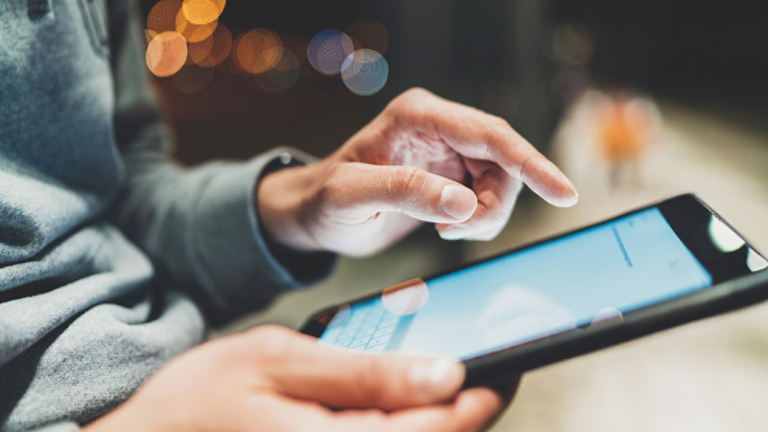 Closeup of male hands using modern digital tablet at night outdoor, technology and social networking concept, hipster guy typing on touch screen of portable computer, bokeh light in blurred background