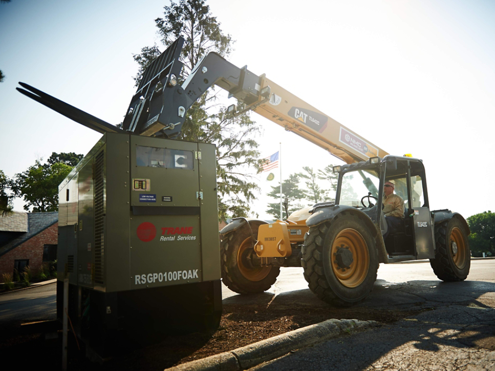 A skid steer loader delivers a Trane Rental Services commercial HVAC unit, which comes with 24/7 technical support.