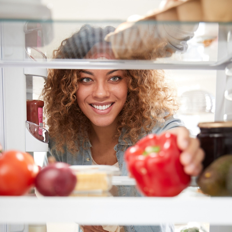 View Looking Out From Inside Of Refrigerator As Woman Opens Door And Unpacks Shopping Bag Of Food