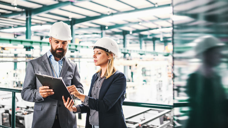A portrait of an industrial man and woman engineer with clipboard in a factory.