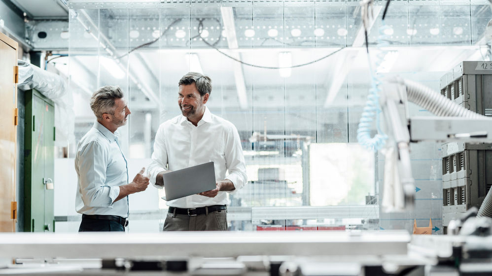 Smiling engineer discussing over laptop with male colleague in factory