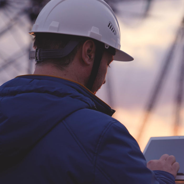 An electrician works in a tablet against a background of energized electrical towers, an engineer measures the level of current, an electrical network to supply light