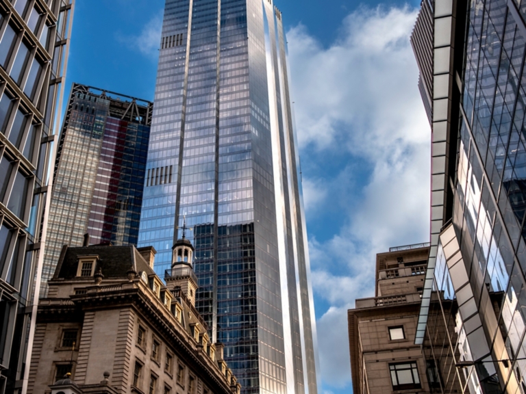 The image showcases a city scene where tall, reflective skyscrapers tower above a historic building, highlighting the intersection of modern innovation and classic architecture  in London UK