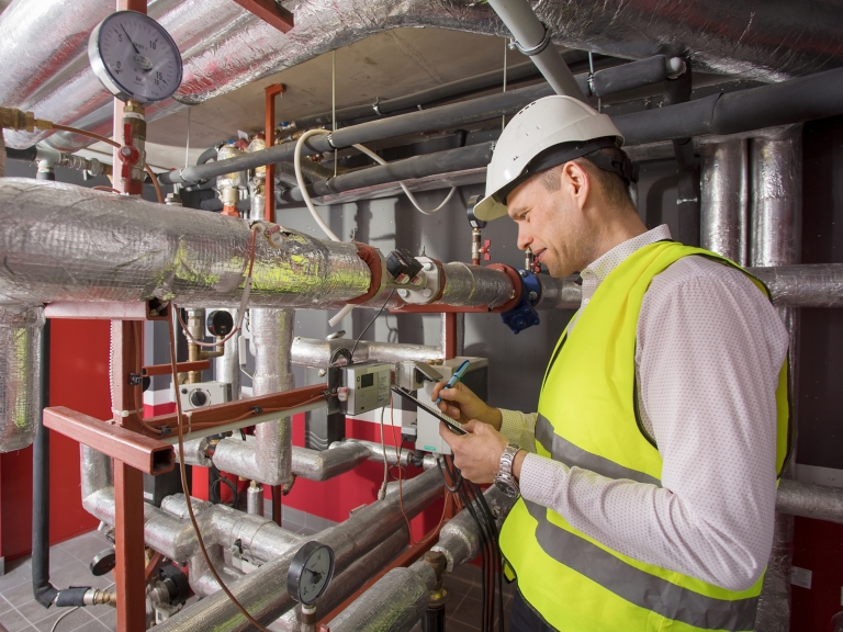Man in helmet writing down measurements in heat and airconditioning system panel
