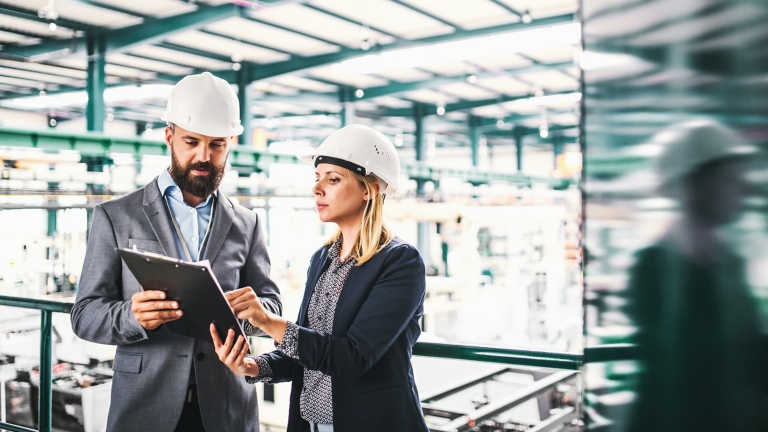 A portrait of an industrial man and woman engineer with clipboard in a factory.