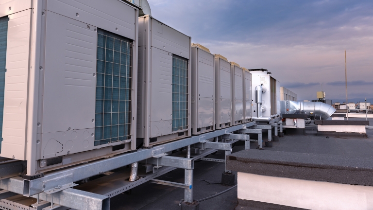 Air conditioner units VRV (HVAC), big fan and a water cooler on a roof of new industrial building with blue sky and clouds in the background.