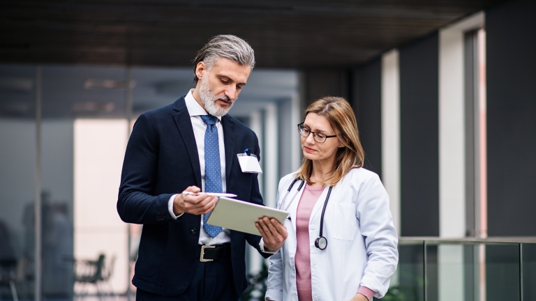 Pharmaceutical sales representative with tablet talking to doctor.