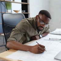 Afro-American architect working in office with blueprints.Engineer inspect architectural plan, sketching a construction project. Portrait of black handsome man sitting at workplace. Business concept