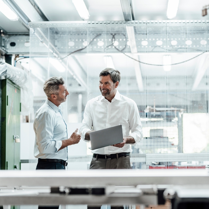 Smiling engineer discussing over laptop with male colleague in factory