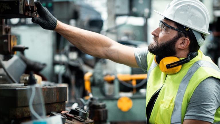 Men industrial engineer wearing a white helmet while standing in a heavy industrial factory behind. The Maintenance looking of working at industrial machinery and check security system setup in fact
