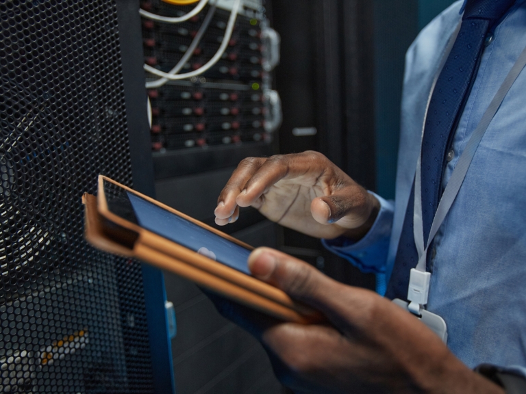 Close up of African American man holding digital tablet while standing by server cabinet and working with supercomputer in data center, copy space