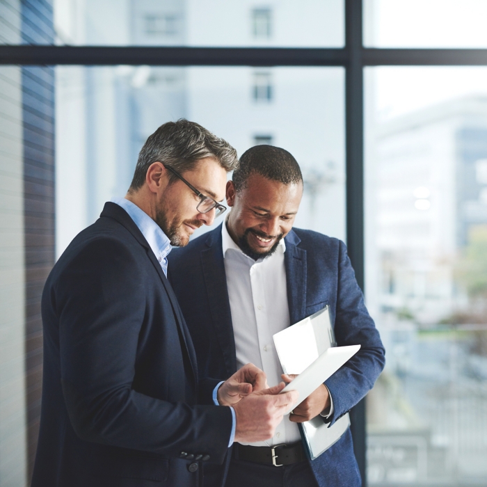 Improving professional performance with the latest apps. Shot of two businessmen using a digital tablet together at work.