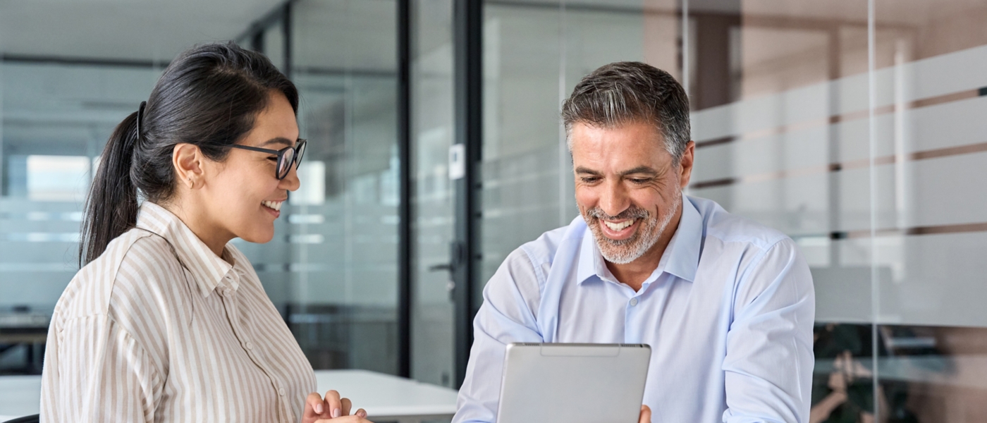 Two happy diverse executives discussing work using digital tablet in office.