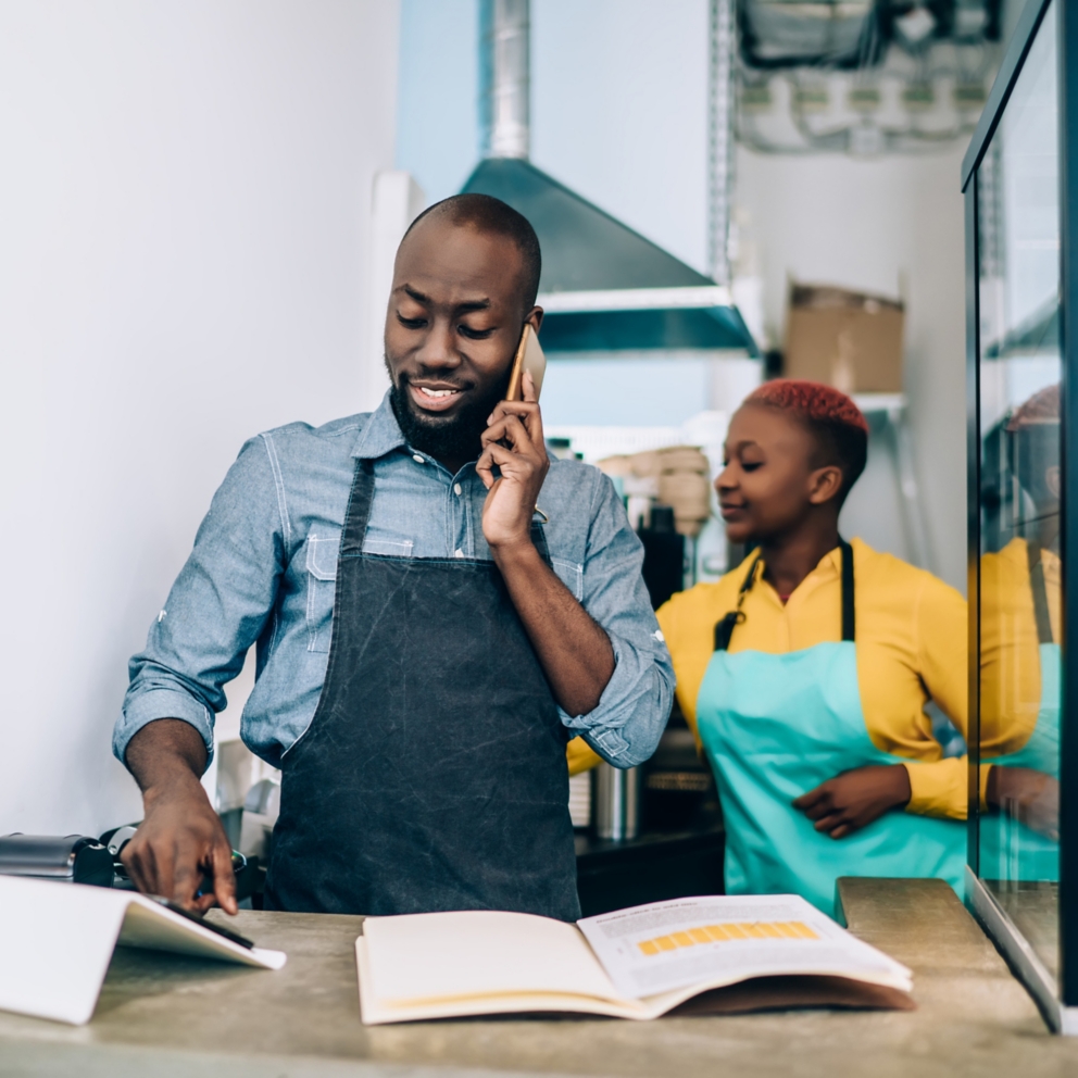 Owner of confectionery shop standing at counter and talking on phone
