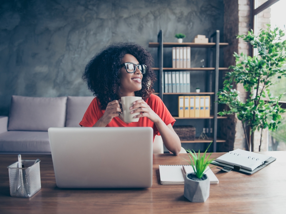 Portrait of dreamy lovely accountant sitting at desk in modern office with interior drinking hot beverage holding cup with tea in hands looking at window enjoying freetime